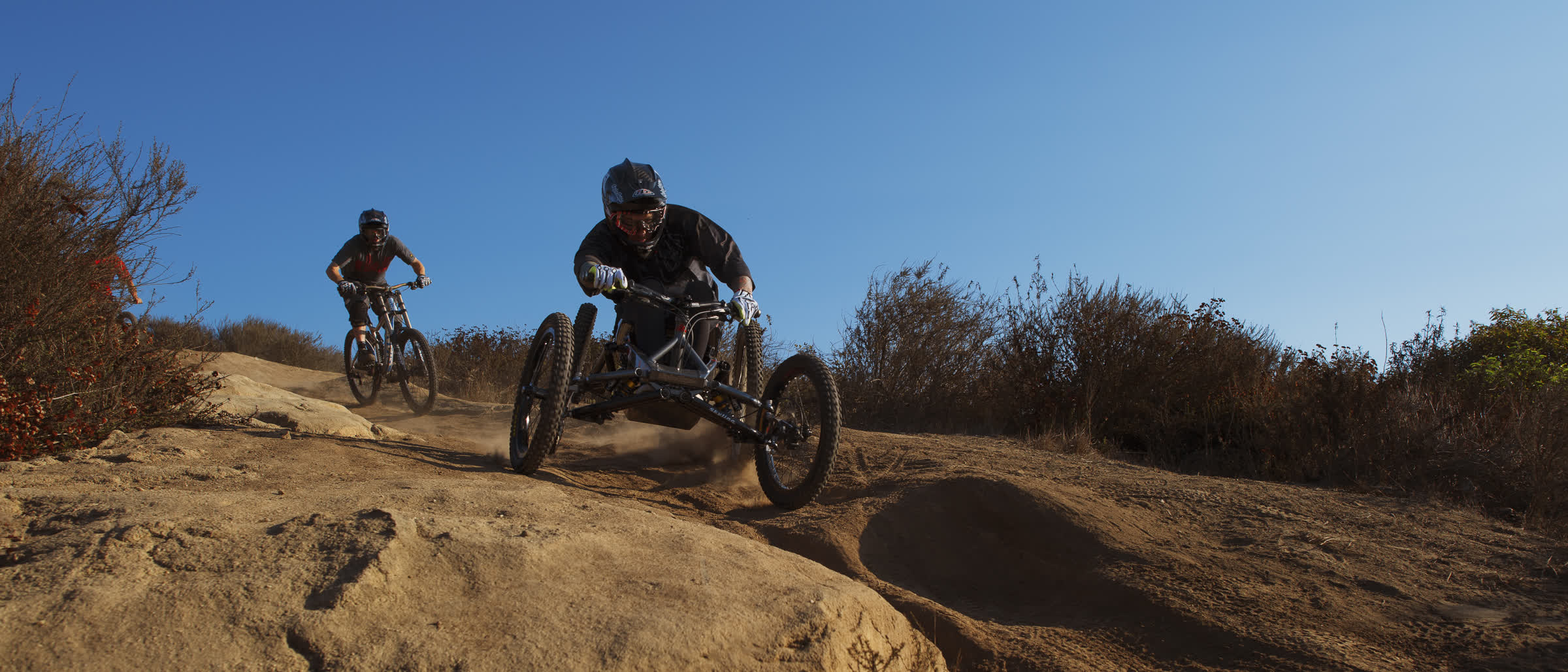 Adaptive mountain bike rider descending a rock face ahead of a standard rider, Active Force Foundation